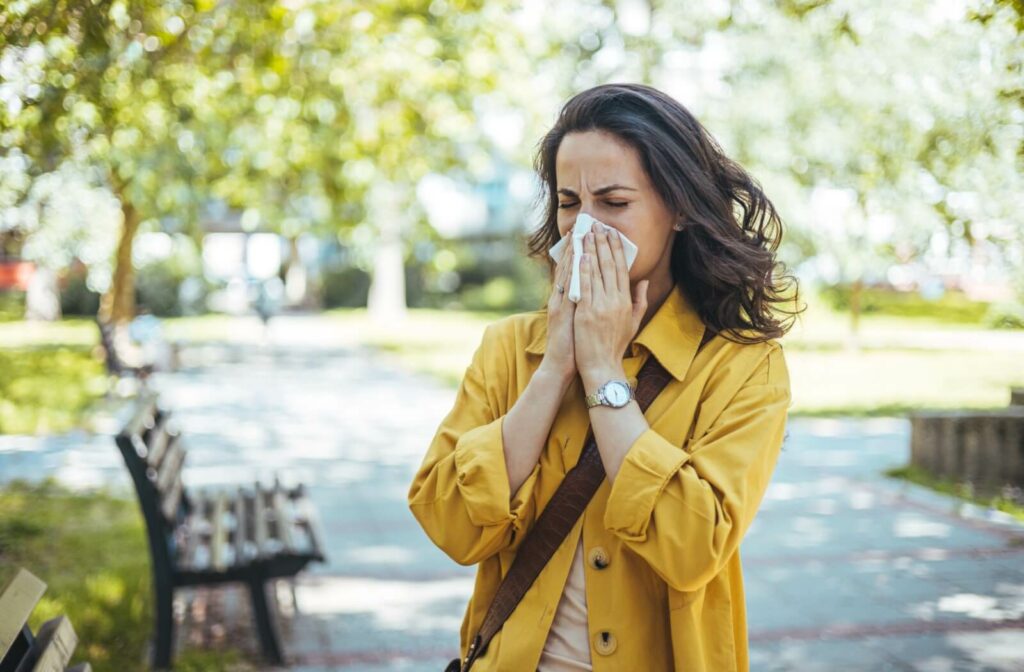 Woman sneezing into a tissue outdoors during allergy season.