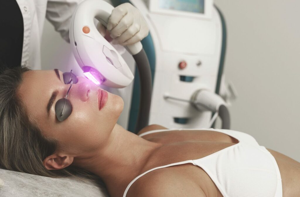 A person receiving IPL treatment with protective eye covers and handheld device emitting light.