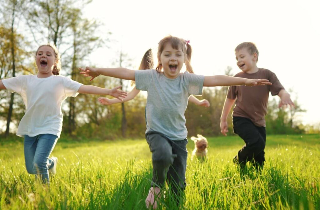 A group of children run through a grassy field on a sunny day.