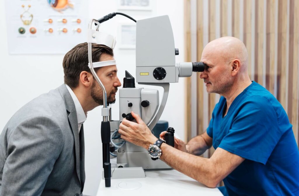 An optometrist in blue scrubs examines an adult patient using a slit lamp during an eye exam.