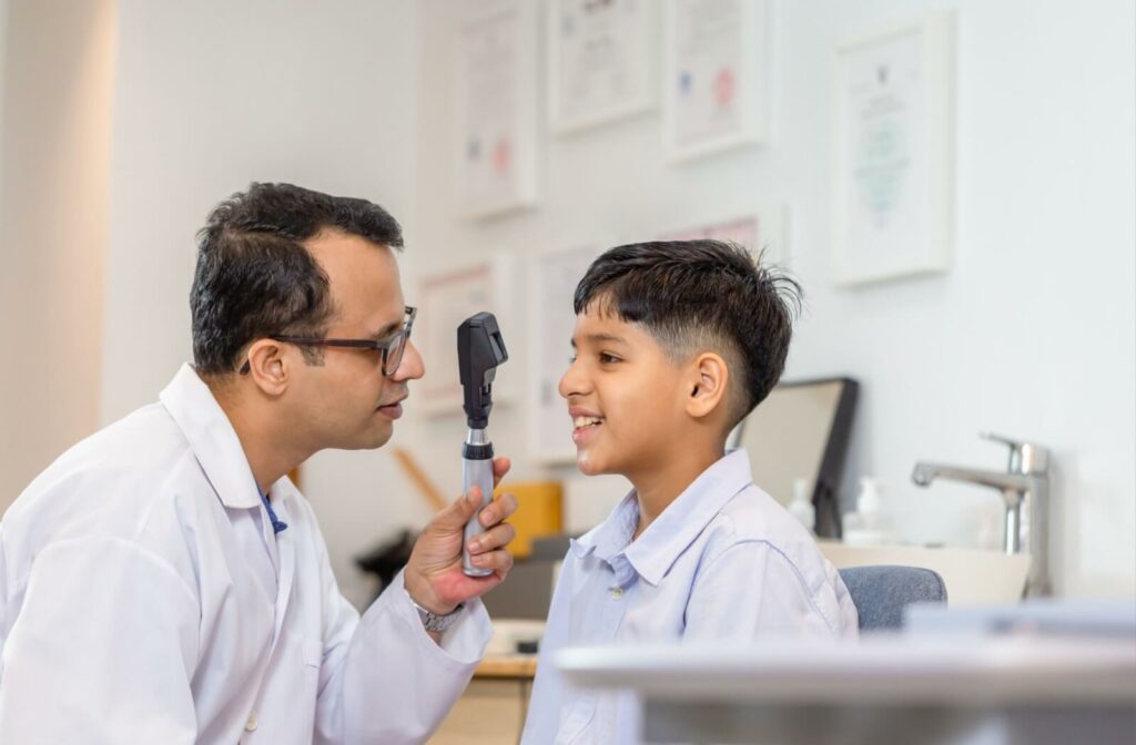 An optometrist in a white coat examines a child's eyes with a handheld light during an eye exam.