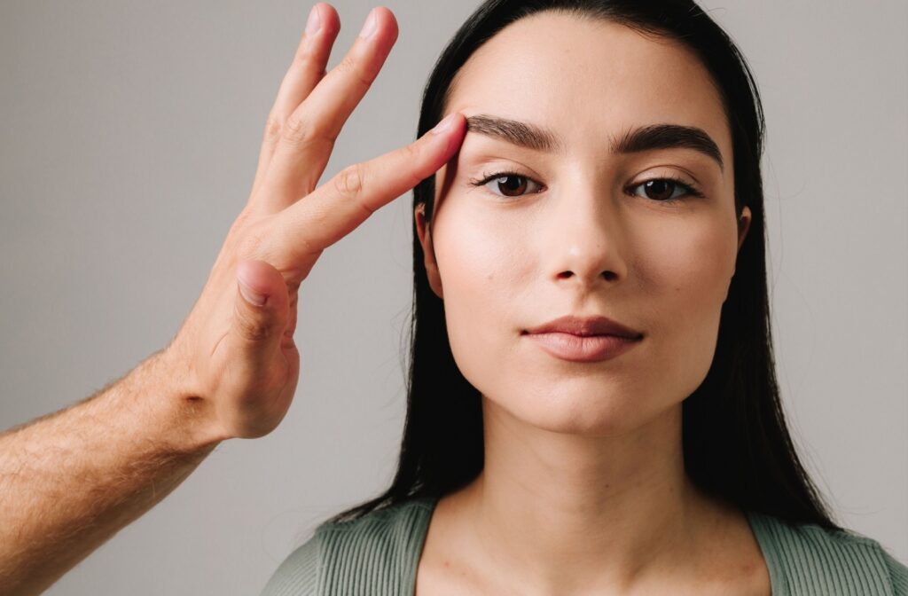 A person gently lifting the outer corner of a woman’s eyebrow to demonstrate the effect of correcting drooping eyelids.